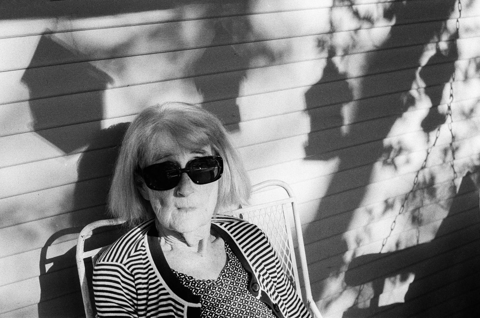 Grandmother on front porch with shadows of bird feeders behind her in afternoon light