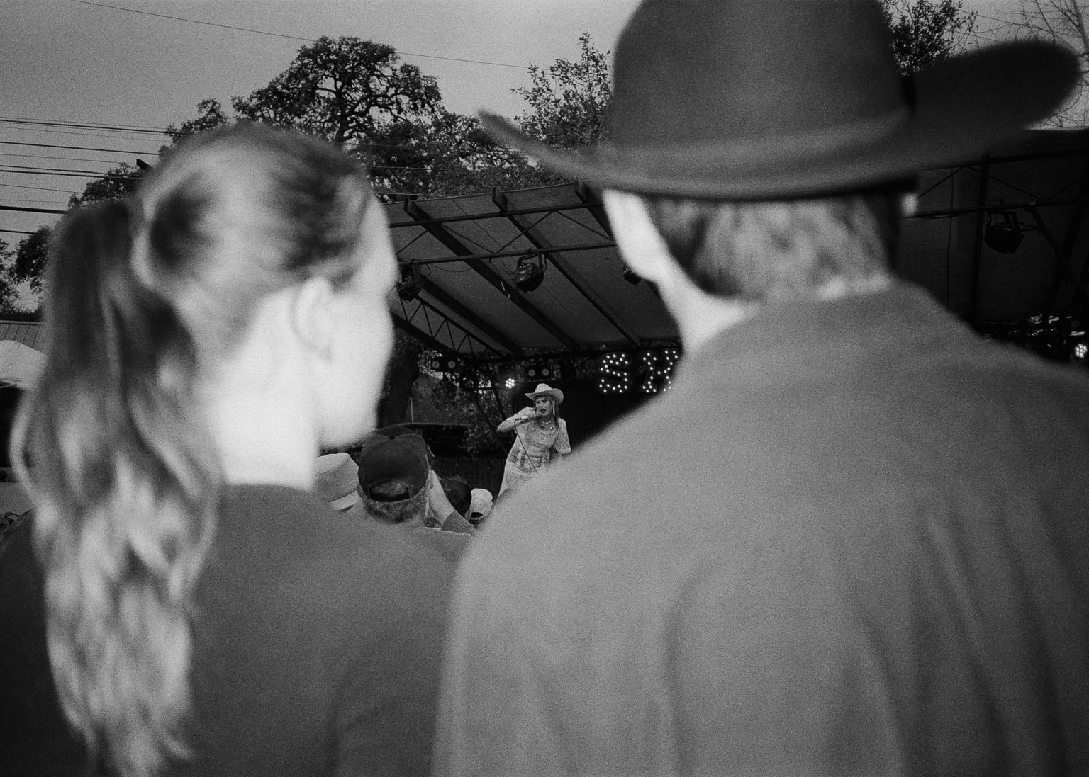 In the crowd between a woman and a man in a cowboy hat off in the distance the lead singer is on stage performing at SXSW in Austion