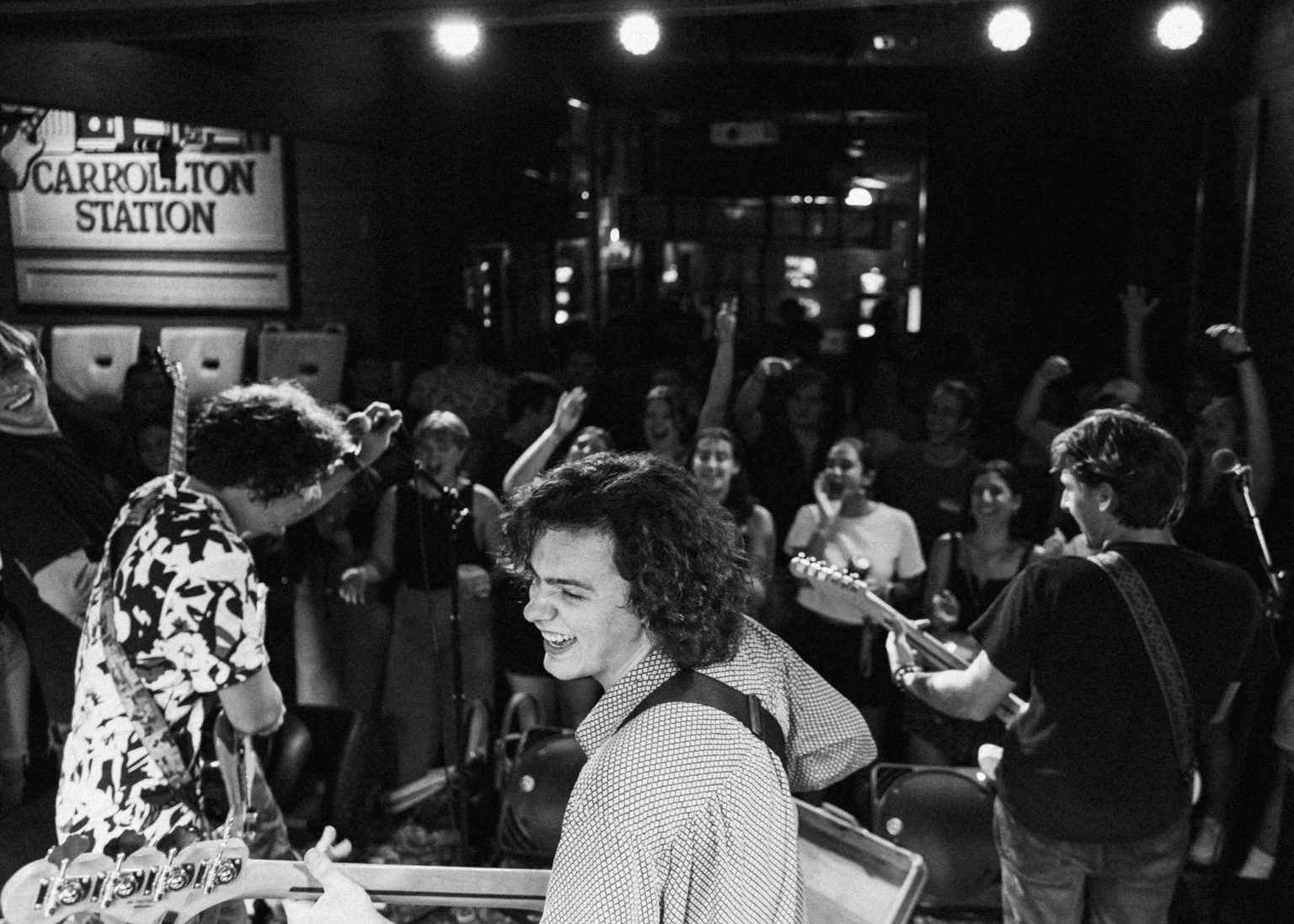 On stage with the Hotel Burgundy Band playing a show crowd cheering them on hands in the air the bassist and lead guitarist looking back smiling