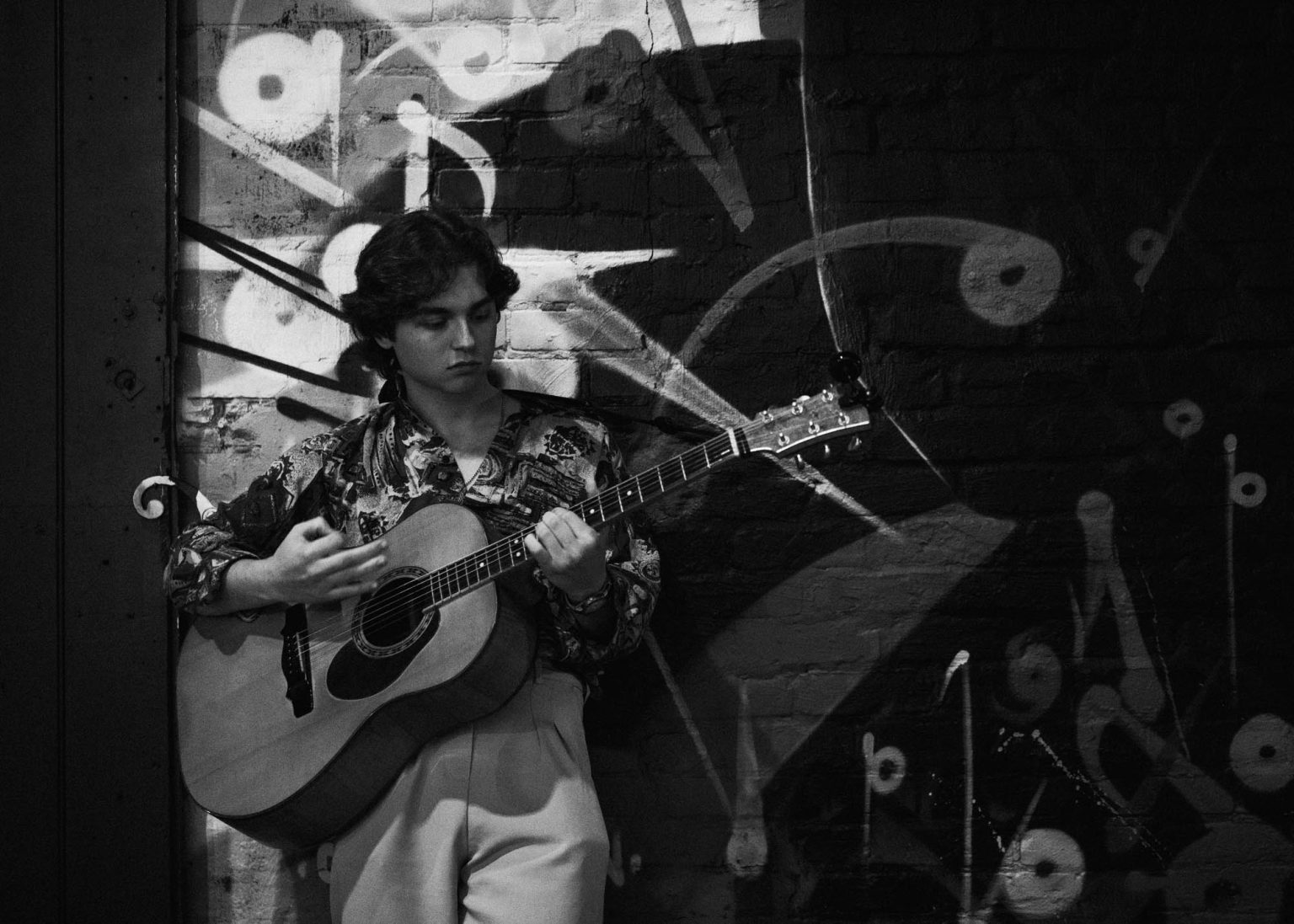 Christian Butler playing his guitar leaning against wall art outside the venue before his show