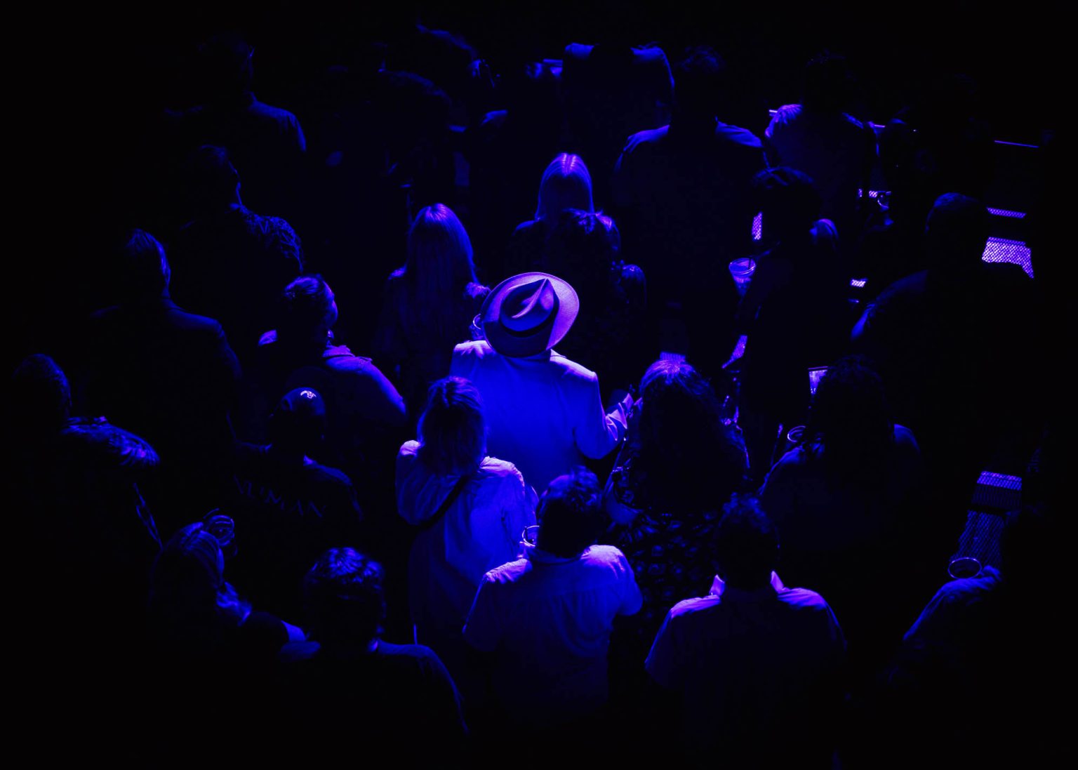 Looking down from the balcony into the crowd stands a man in a cowboy hat