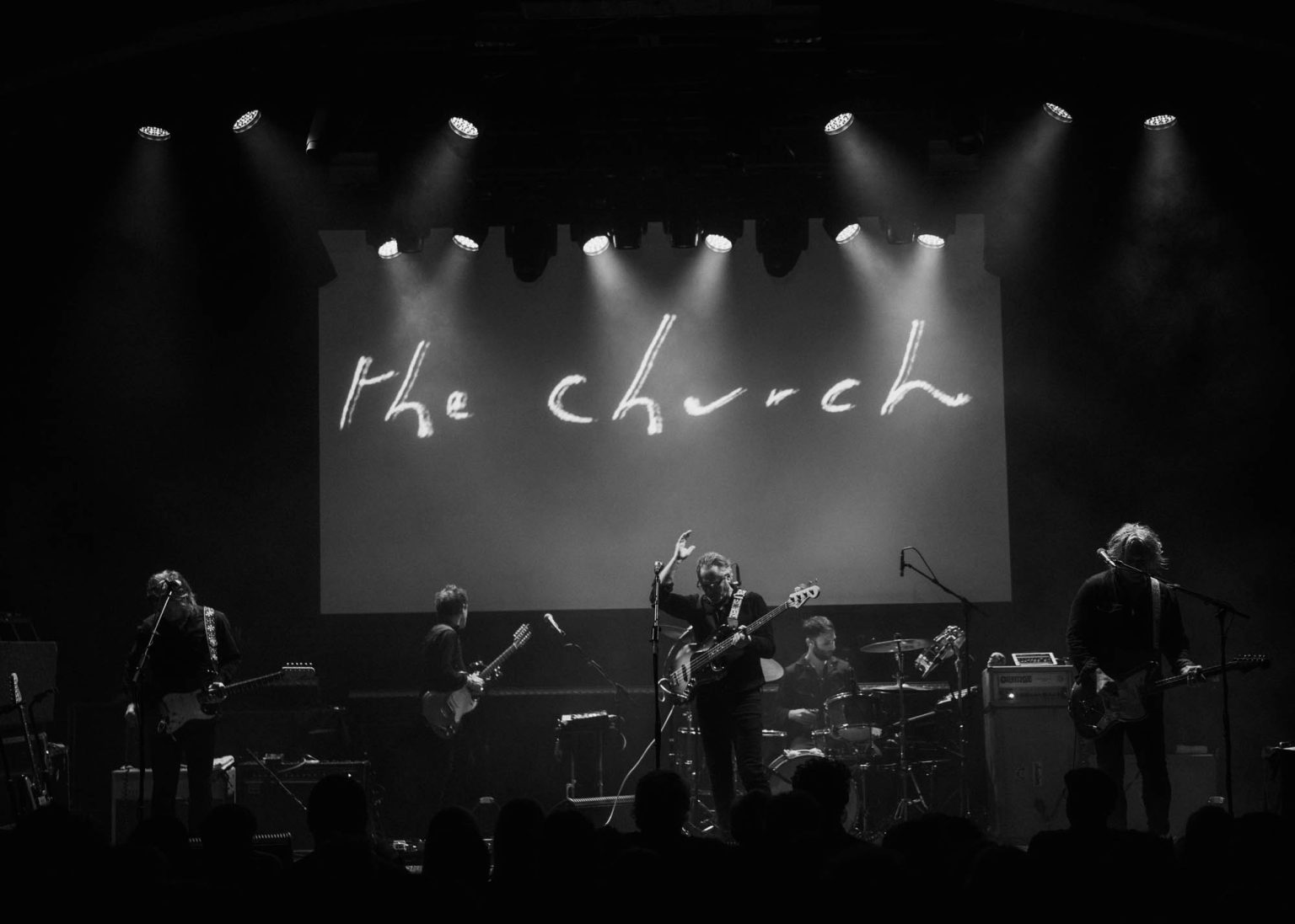 The whole band of The Church on stage with their logo being projected beind them