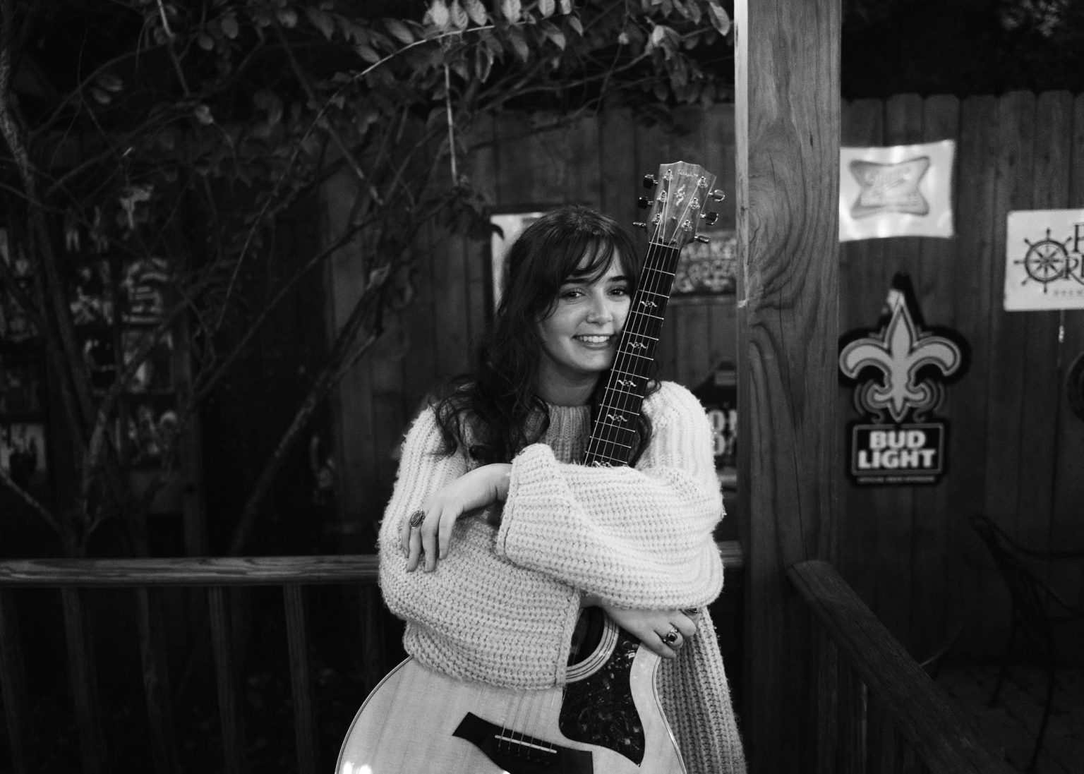 Olivia Barnes holding her guitar and smiling on the patio at the Carrollton Station in New Orleans