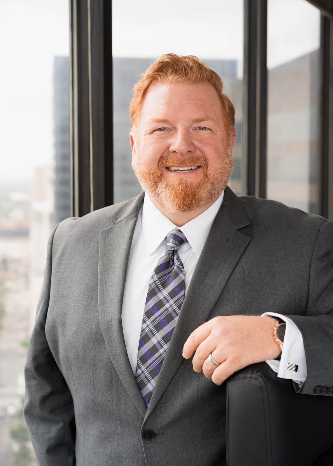 Lawyer in suit smiling in downtown high rise with his arm on chair