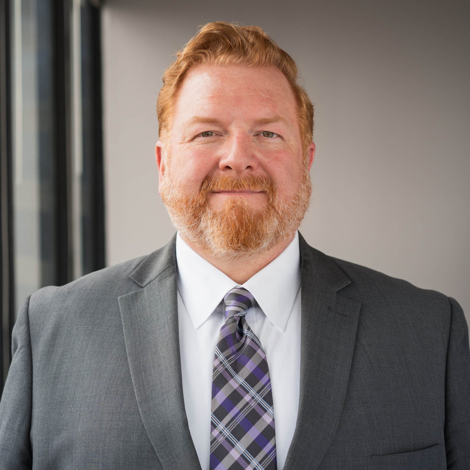 Lawyer smiling in downtown office building with windows at his side while wearing a suit