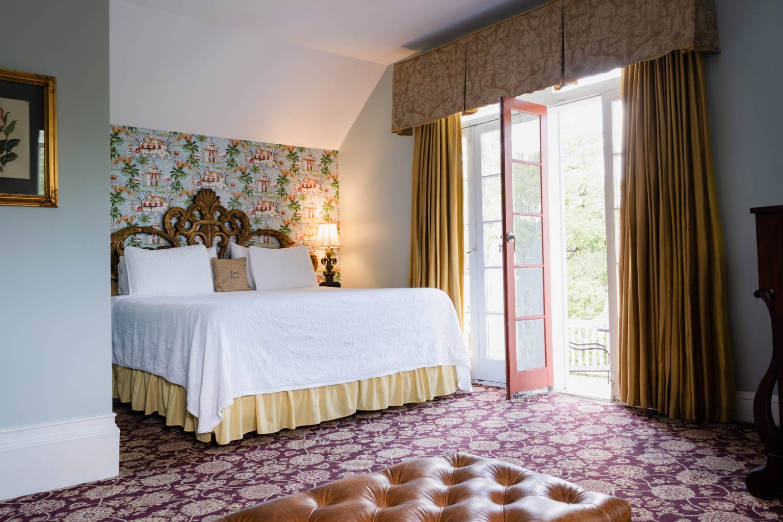 Hotel bedroom in afternoon light with a large window and open door that leads onto a balcony