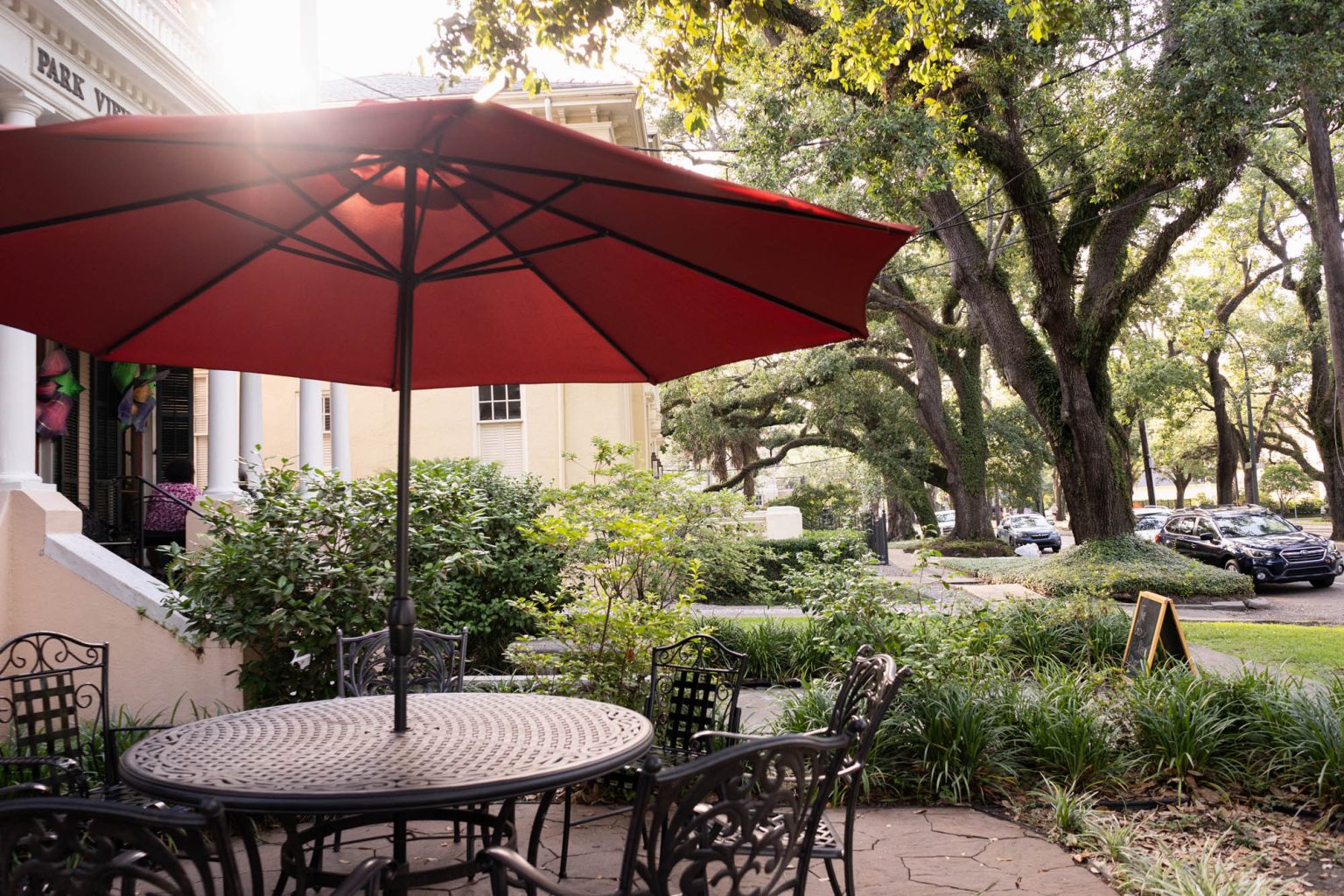 Seating area in front of hotel with red umbrella overhead in afternoon light