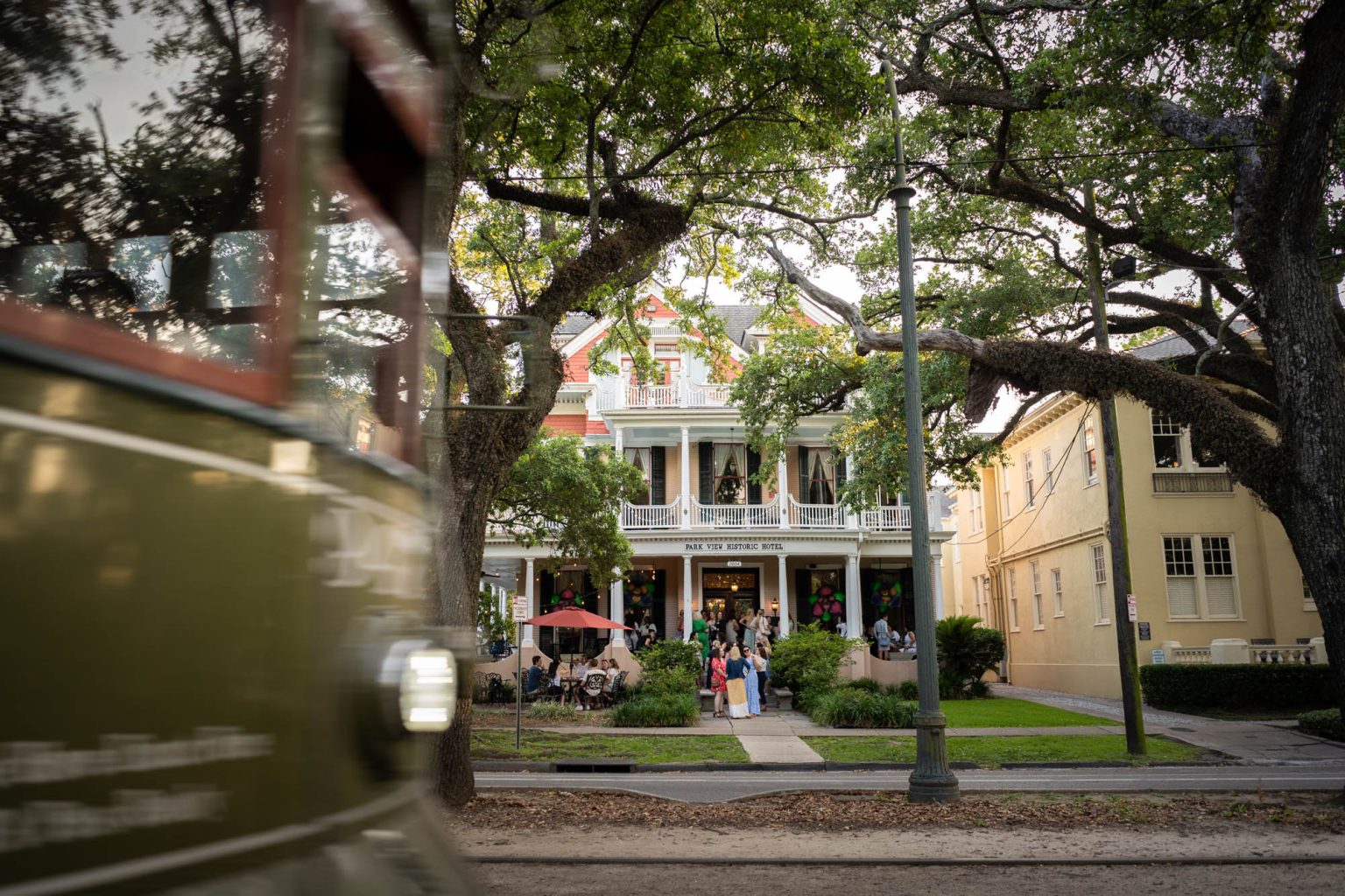 New Orleans streetcar passing in front of hotel as guests hang out on the front porch with drinks from hotel bar