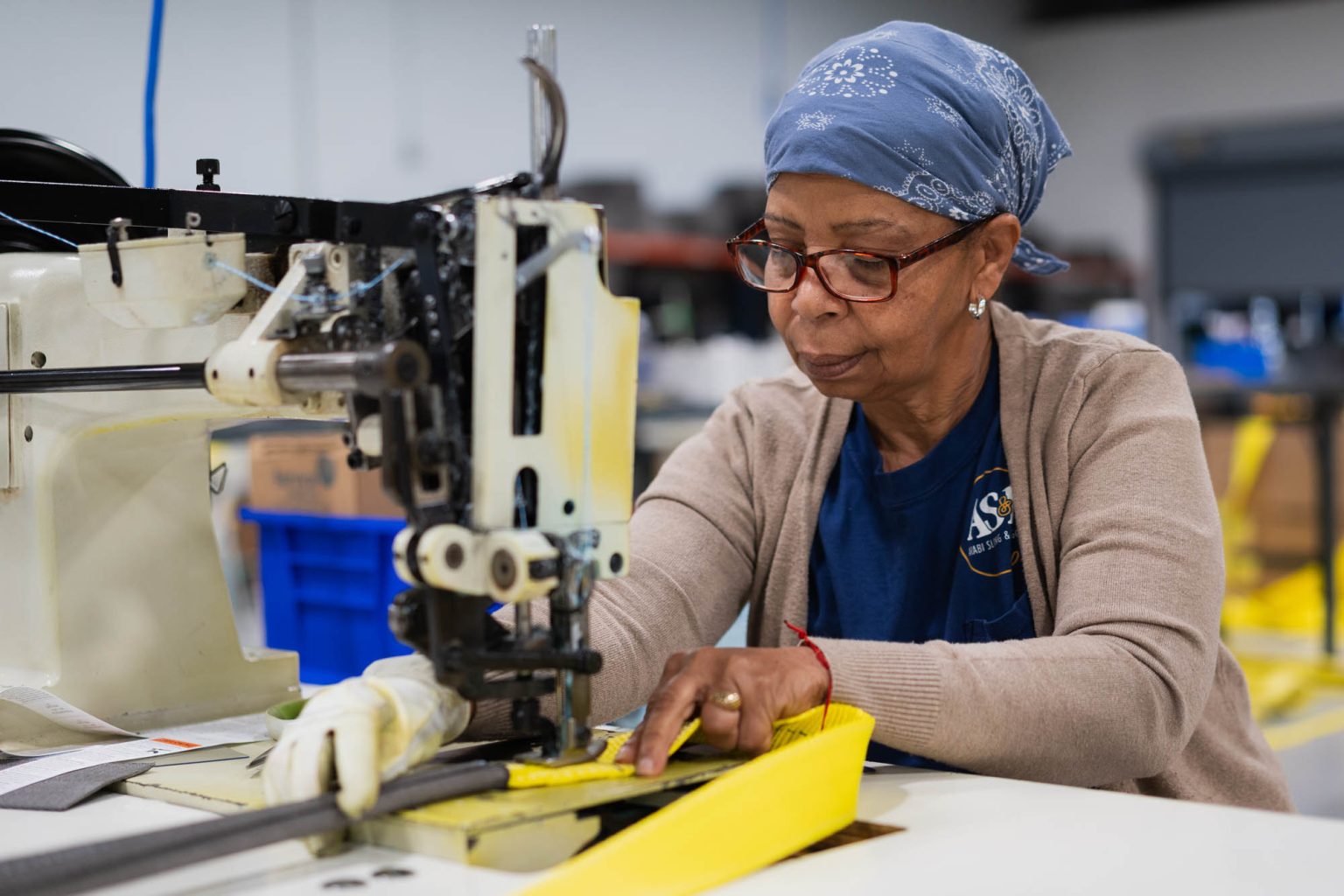 Smiling and working on crafting yellow sling products at the sewing machine