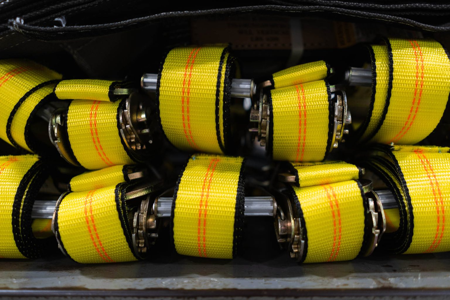 Stack of yellow ratchet straps with orange threading on shelf