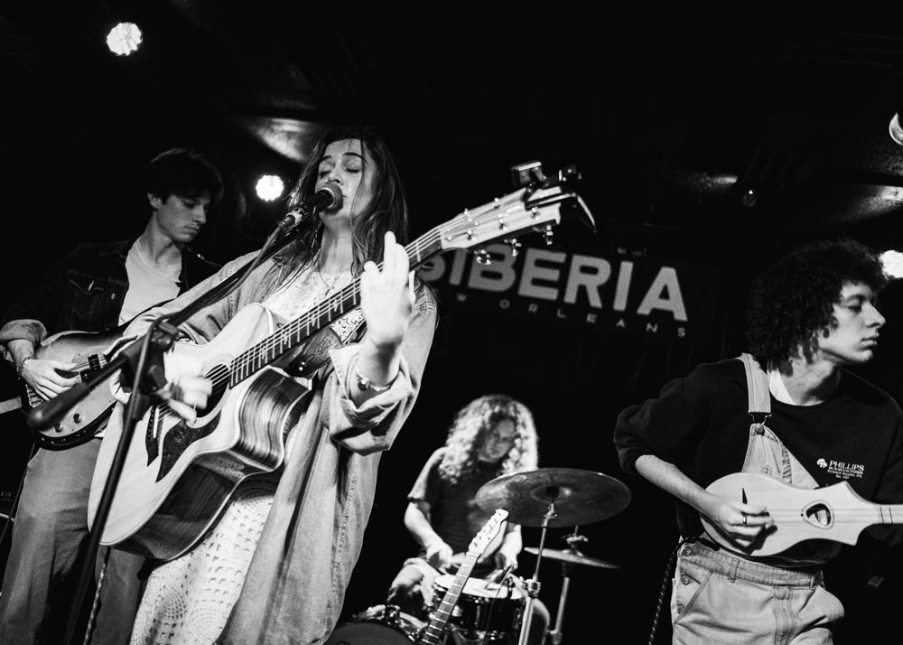 Olivia Barnes Band on stage all playing a concert together including drums, bass, and acoustic guitars