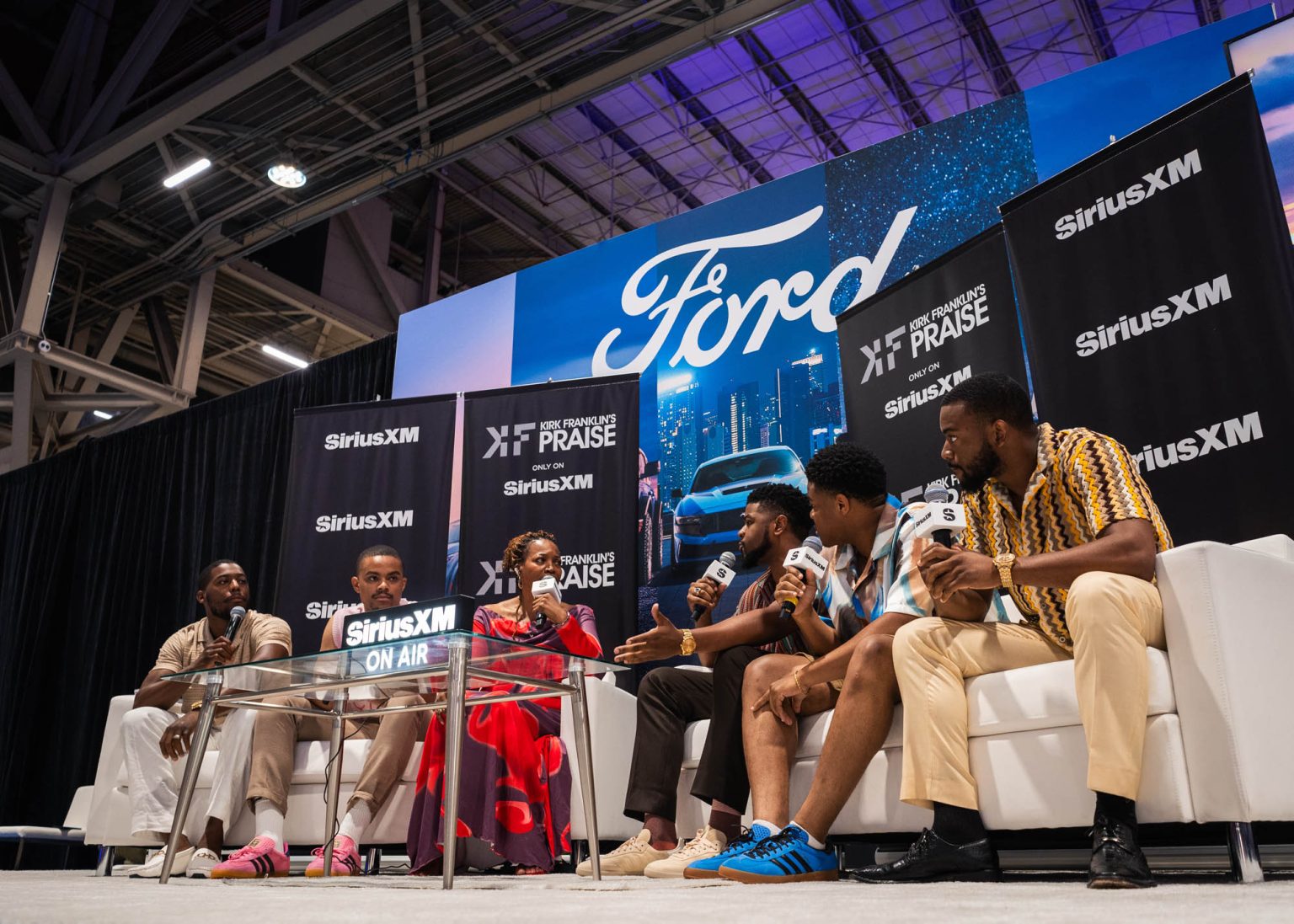 Group on stage siting on couches for an interview before their live on stage performance