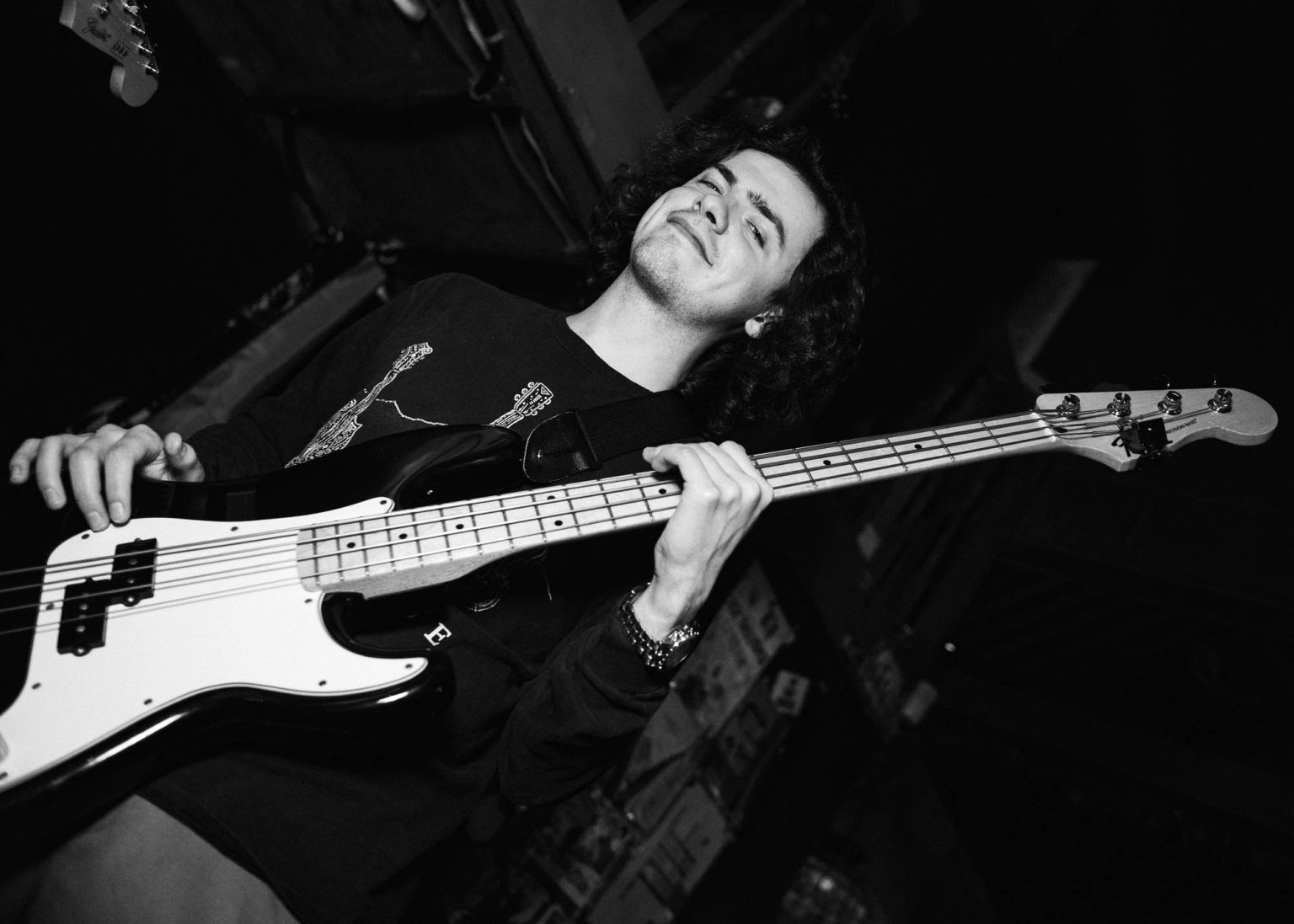 Bassist smiling and tilting his bass guitar up during a concert him and his band are performing at a local bar