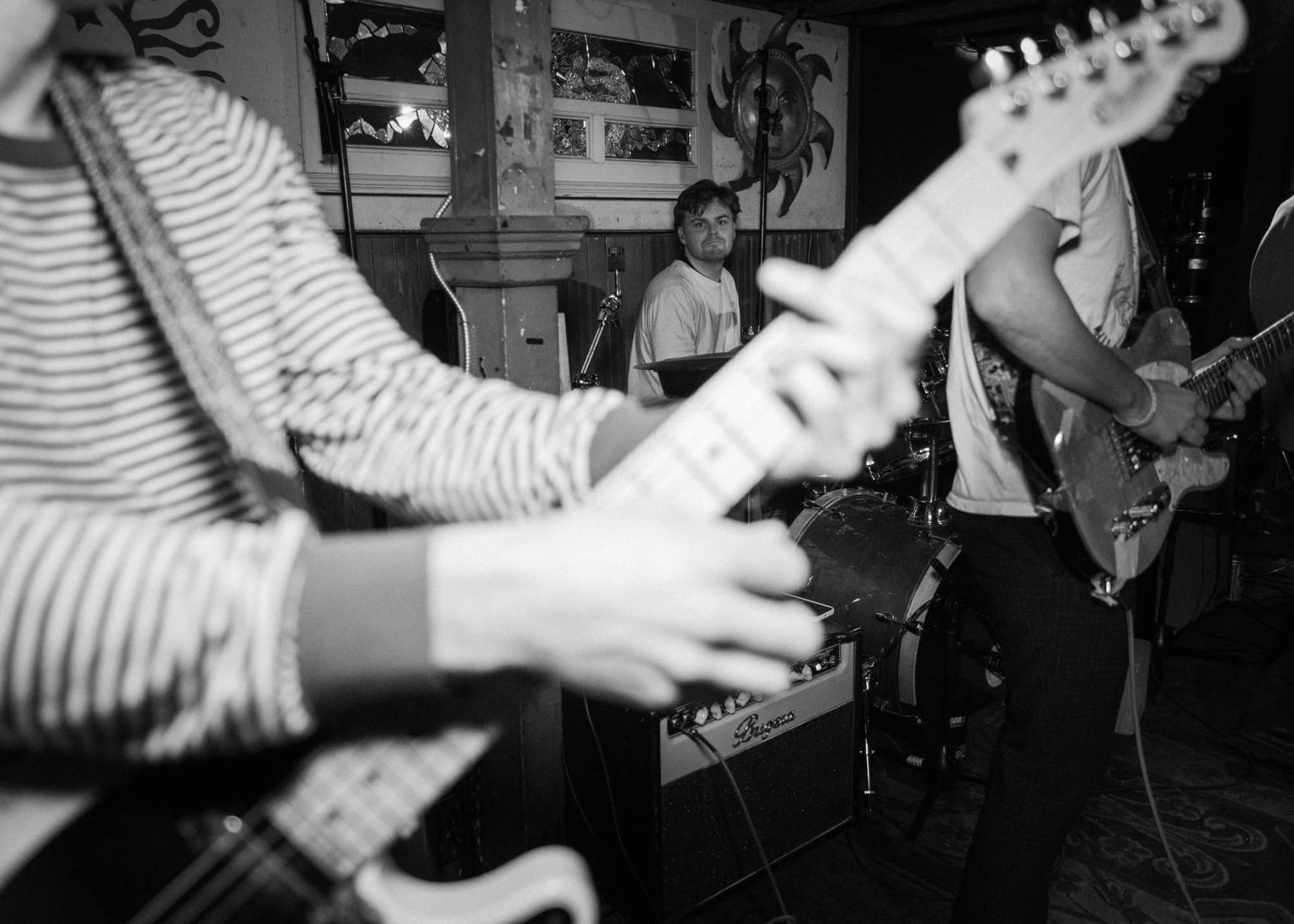 Guitarist holding up guitar and drummer in the background smiling during their live performance at a local bar