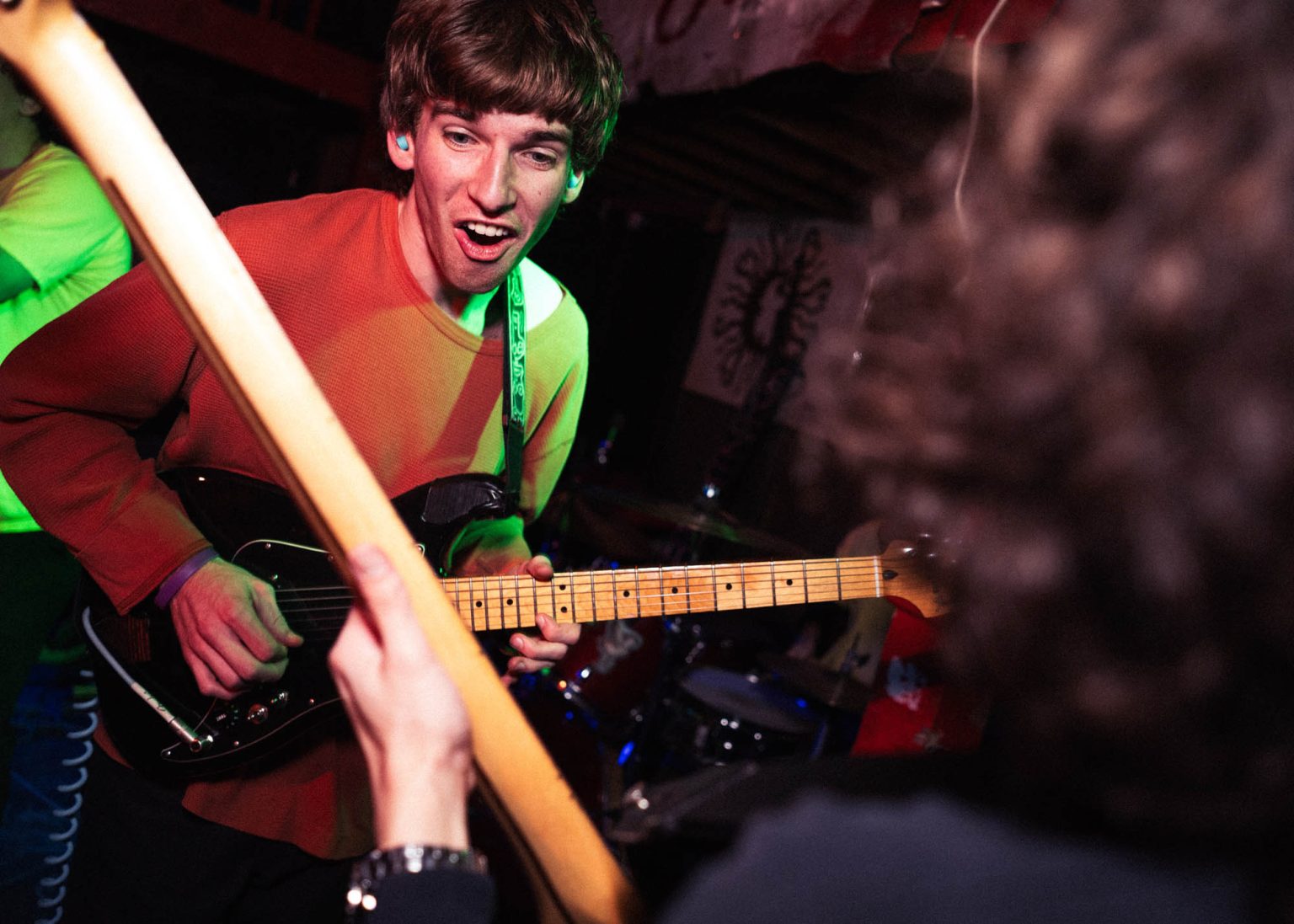 Guitarist smiling at bassist holding up his bass guitar while on stage at a local venue