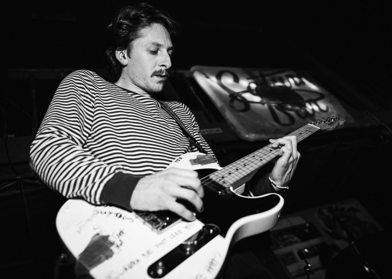 Guitarist playing notes on his guitar while wearing a black and white striped shirt during their live performance