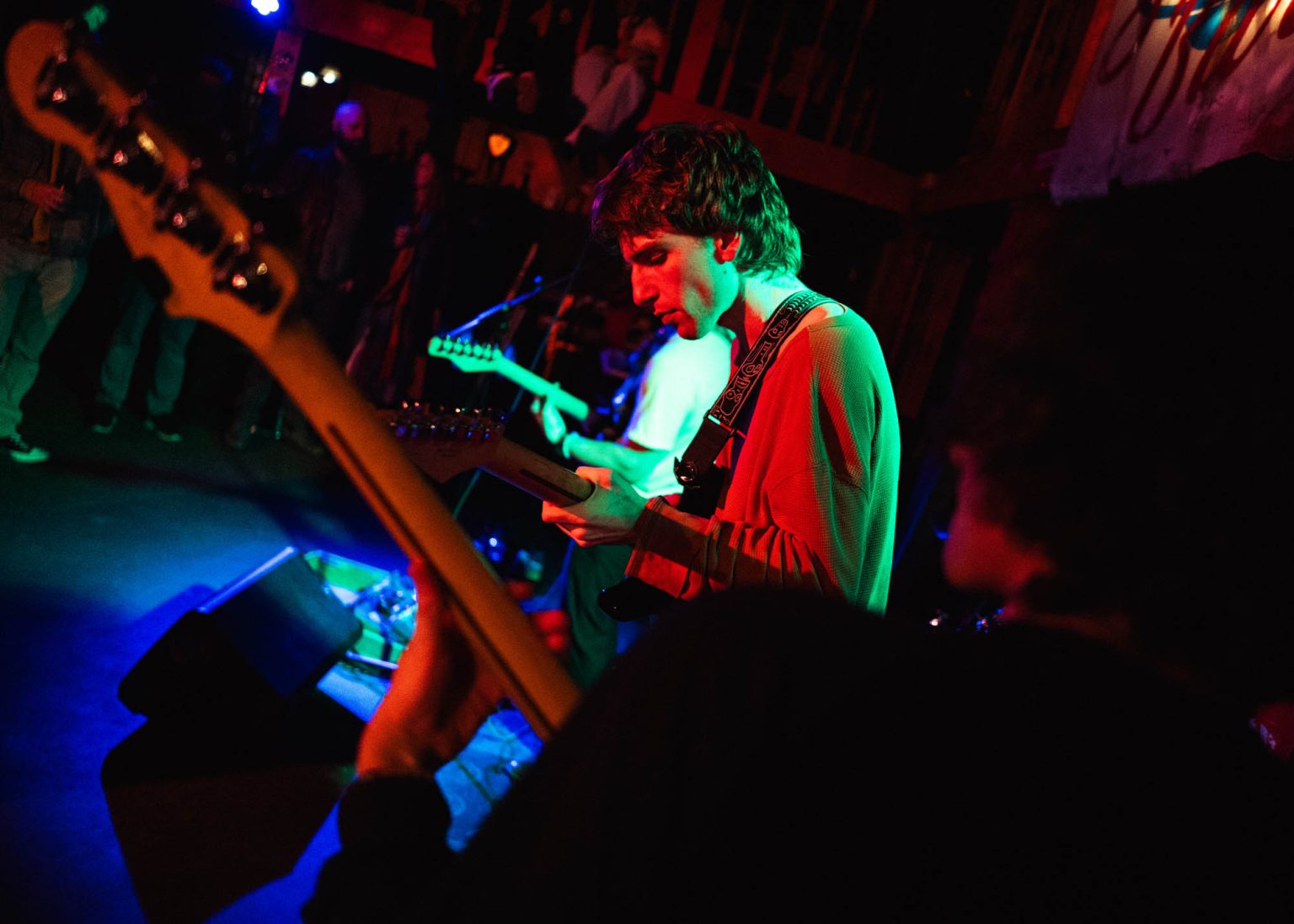 Bassist in the foreground with guitarist Evan in the mid-ground playing guitar and fellow guitarist in the background along with crowd