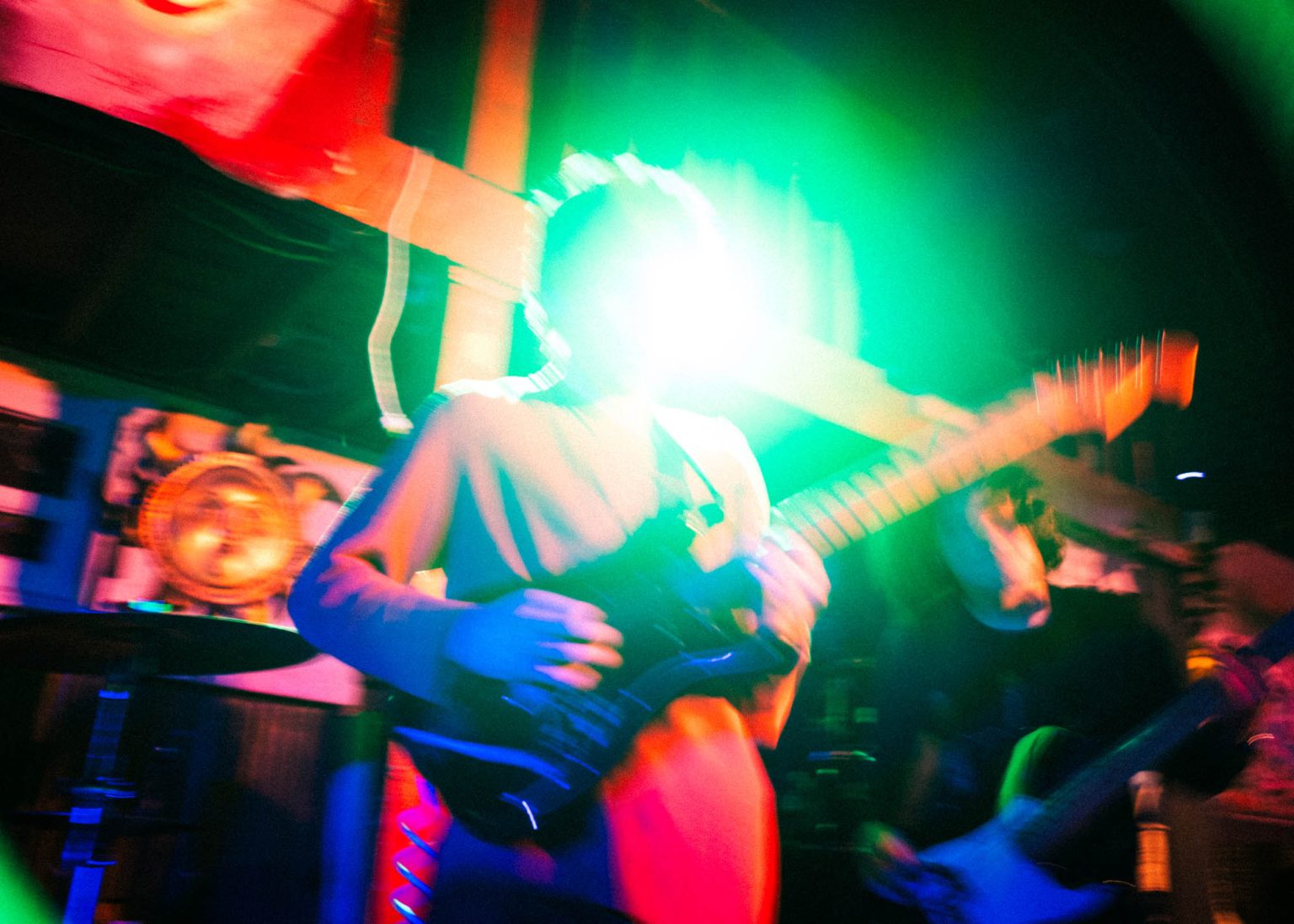 Guitarist on stage with bassist and bright green stage light behind him