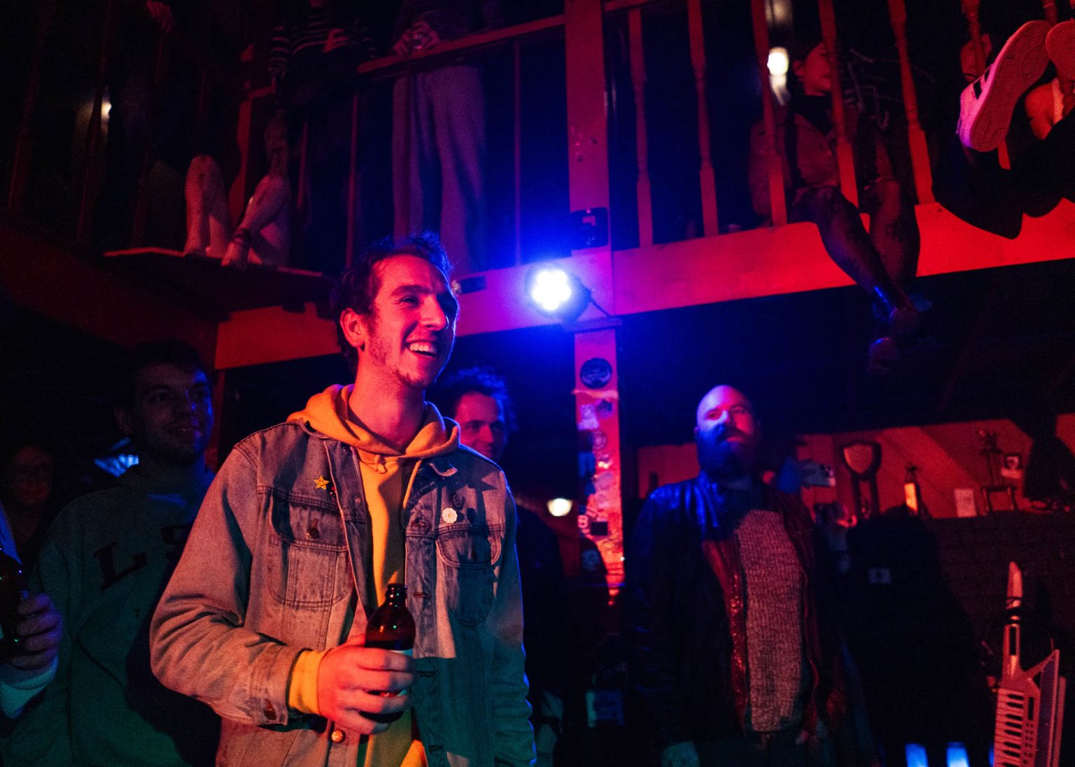 Guy in crowd smiling along with other people in the crowd as he watches the band Hotel Burgundy play on stage at Saturn Bar