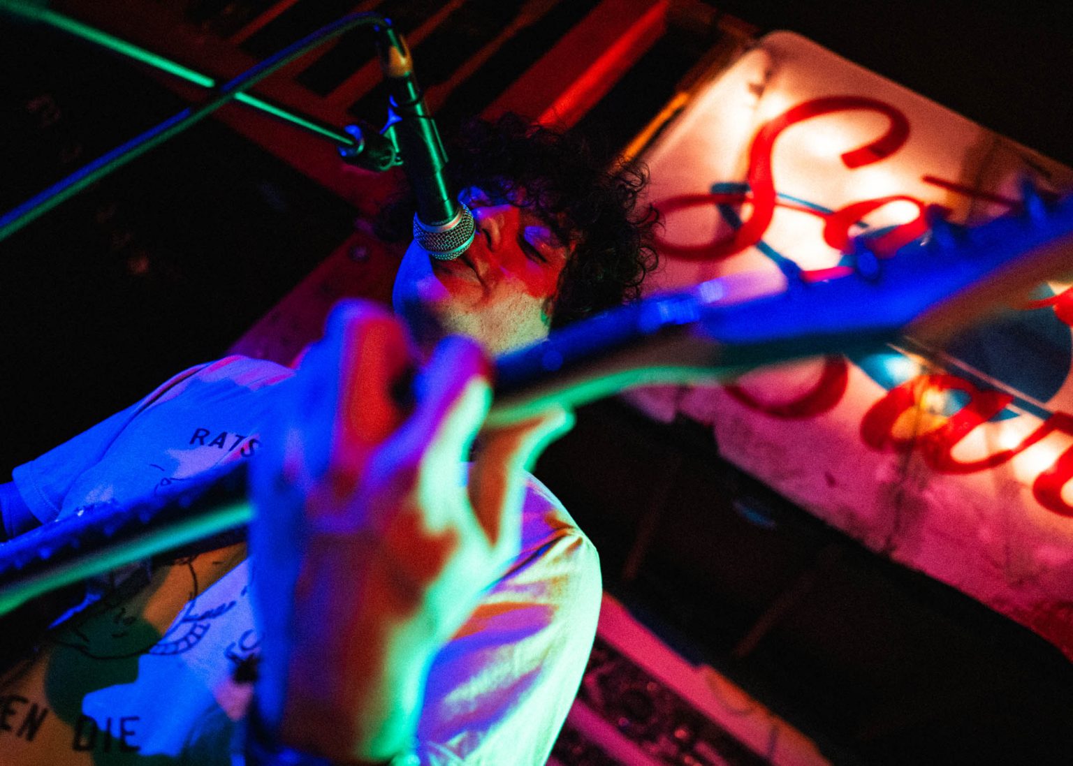 Lead singer playing guitar on stage with the sign of the music venue in the background Saturn Bar