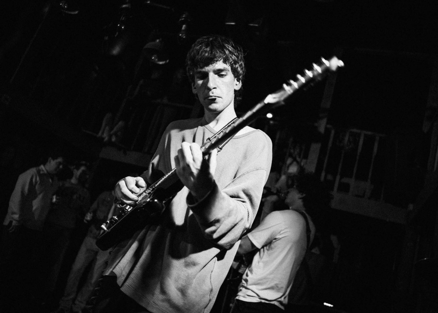 Guitarist plays guitar with lead singer and crowd in the background