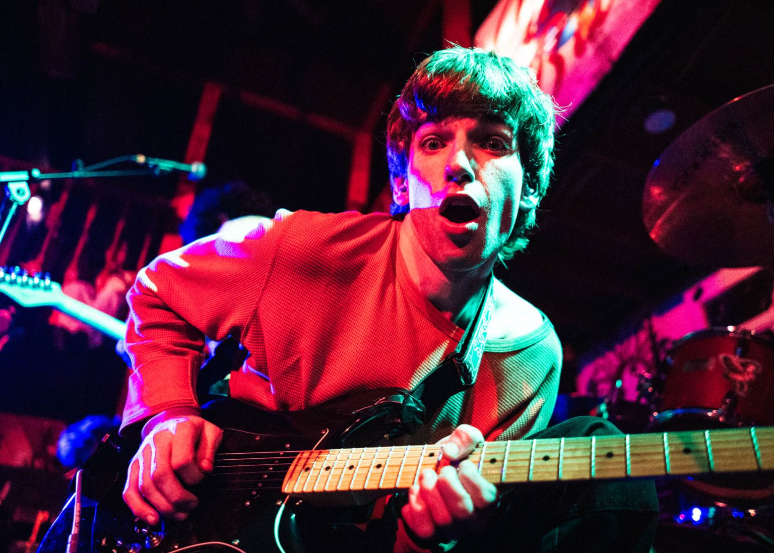 Guitarist Evan of the band Hotel Burgundy crouched down playing the guitar making a silly face