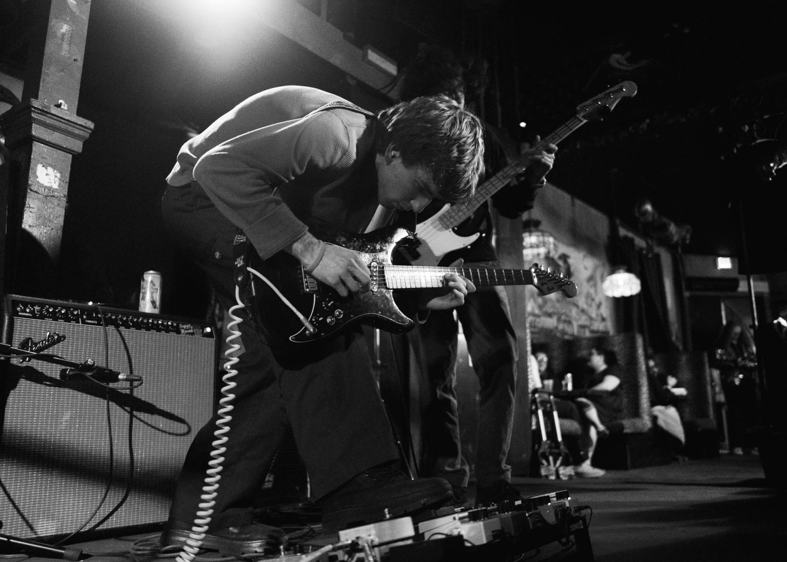 Guitarist crouched playing guitar focused on playing the guitar with bassist in the background