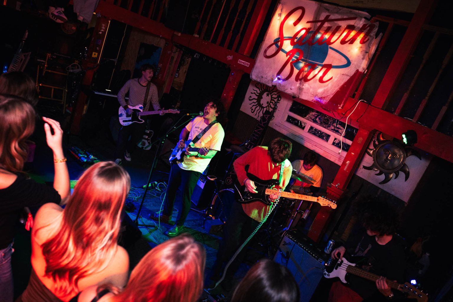 Crowd in the foreground and band on stage playing instruments and sign of the music venue above them Saturn Bar