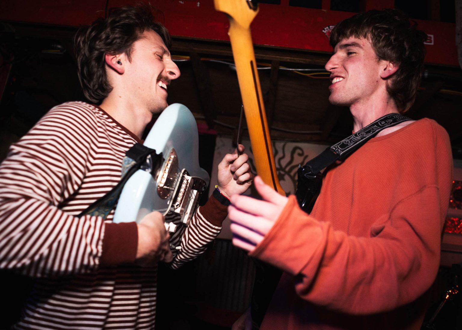 The two guitarists of Hotel Burgundy on stage laughing together during their concert