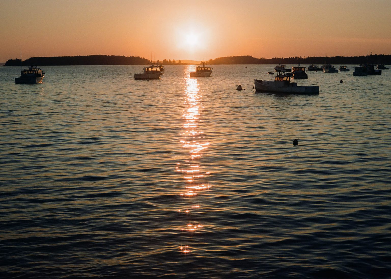 Sun near the horizon with lobster boats on the water at a harbor in Maine